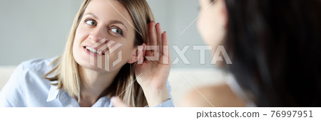 Young woman holding her ear and talking to friend 76997951