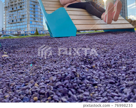 A woman in beautiful sportswear with pink sneakers on her feet sits on a fashionable new bench lounger in the park with purple pebbles for landscape design A woman in beautiful sportswear with pink sneakers on her feet sits on a fashionable new bench lounger in the park with purple pebbles for landscape design 76998233