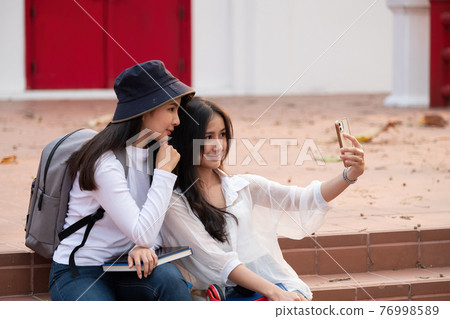 Two students with beaming smiles are posing for selfie shot, Asian attractive lady is taking in university or campus. Two students with beaming smiles are posing for selfie shot, Asian attractive lady is taking in university or campus. 76998589