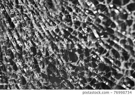 Black-and-white Texture of broken glass on dark background. Closeup 76998734