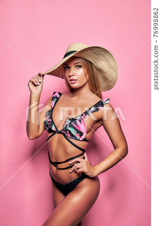 A gorgeous trendy fit woman in swimwear and hat while she enjoying rest with sunlight isolated over pink background. Travel, tourism, journey, trip, tour, summer concept A gorgeous trendy fit woman in swimwear and hat while she enjoying rest with sunlight isolated over pink background. Travel, tourism, journey, trip, tour, summer concept 76998862