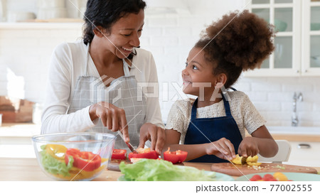 Happy mom and daughter kid talking and laughing while cooking 77002555
