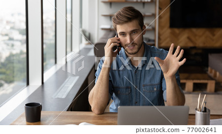 Young Caucasian businessman work on laptop talk on smartphone Young Caucasian businessman work on laptop talk on smartphone 77002641