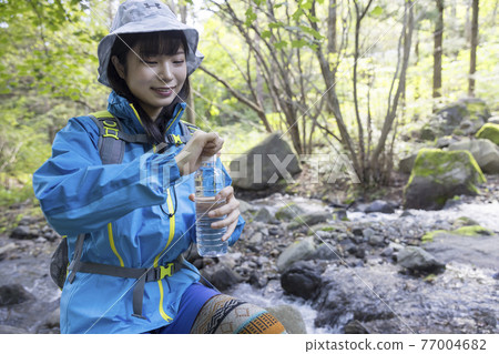 Trekking image of a young woman opening the lid of a PET bottle in the mountains Trekking image of a young woman opening the lid of a PET bottle in the mountains 77004682