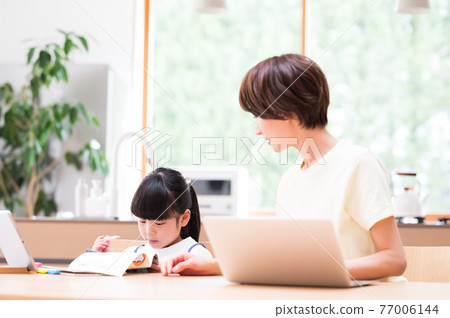 A girl learning at the kitchen table with the support of her mother 77006144