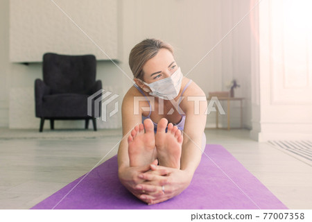 Young woman in protective mask doing yoga, stay isolation at home for self quarantine. 77007358
