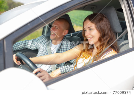 Cheerful girl driving car with boyfriend in passenger seat Cheerful girl driving car with boyfriend in passenger seat 77009574
