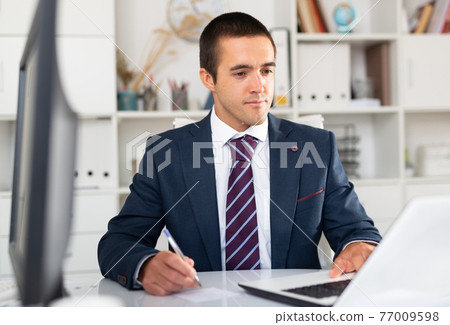 Busy entrepreneur at office desk with papers and laptop Busy entrepreneur at office desk with papers and laptop 77009598