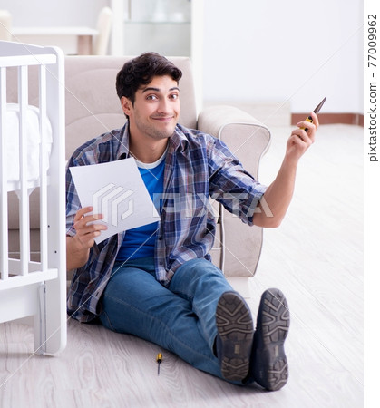 Young man assembling baby bed with instruction manual 77009962