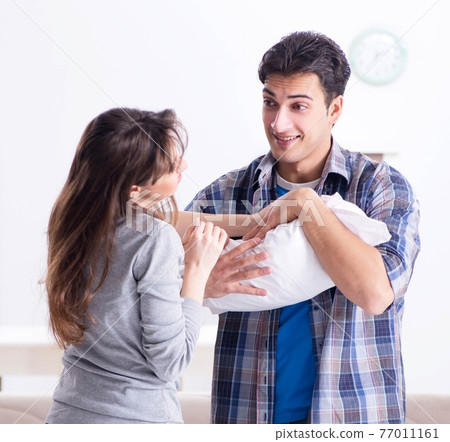 Young parents with their newborn baby near bed cot 77011161