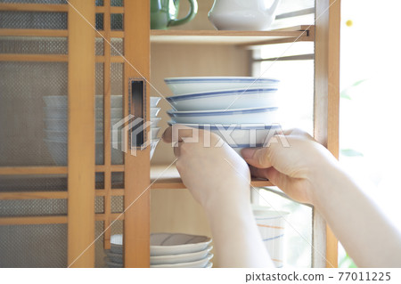 Female hand taking dishes out of the cupboard Female hand taking dishes out of the cupboard 77011225