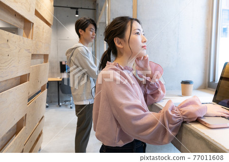 一位年輕女子站在共享辦公空間，在電腦上工作 77011608