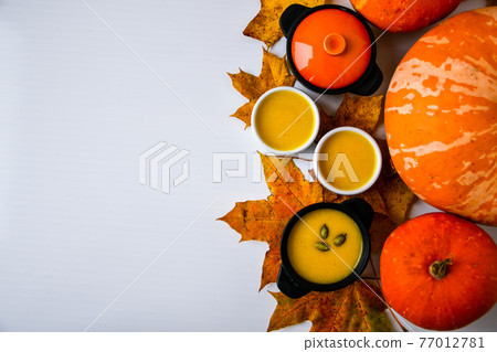 Autumn food. Frame of pumpkin puree soup, leaves. Top view. Autumn harvest, pumpkins, leaves on grey as abstract background. Thanksgiving day. Flat lay. Copy space Autumn food. Frame of pumpkin puree soup, leaves. Top view. Autumn harvest, pumpkins, leaves on grey as abstract background. Thanksgiving day. Flat lay. Copy space 77012781