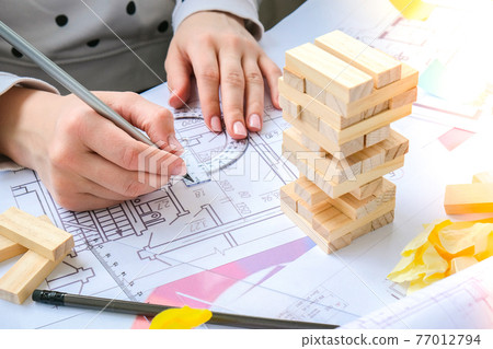 Architect designer Interior creative working hand playing a block wood game on desk architectural plan of the house, a color palette. Female architect drawing blueprints in office workplace. 77012794
