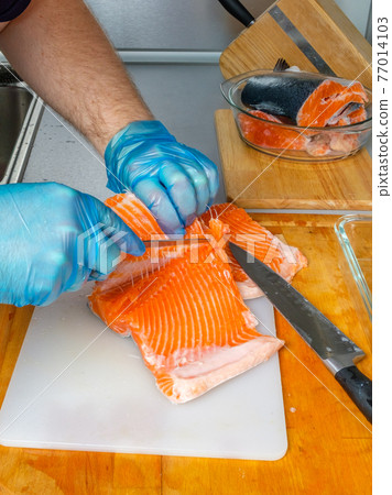 The hands of the cook separate the salmon fillets from the bones with a knife. The hands of the cook separate the salmon fillets from the bones with a knife. 77014103