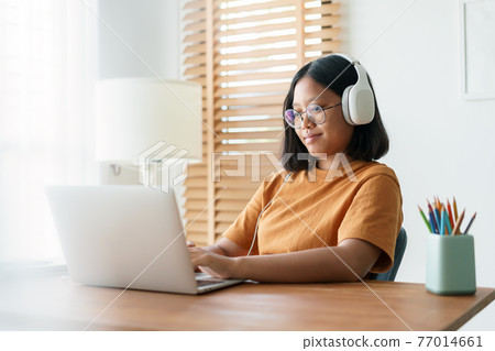 Asian student woman learning online using a computer laptop with headphones while sitting workplace Asian student woman learning online using a computer laptop with headphones while sitting workplace 77014661