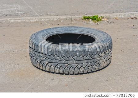 Thrown out on a deserted road, an old, worn-out winter tire from a car wheel Thrown out on a deserted road, an old, worn-out winter tire from a car wheel 77015706