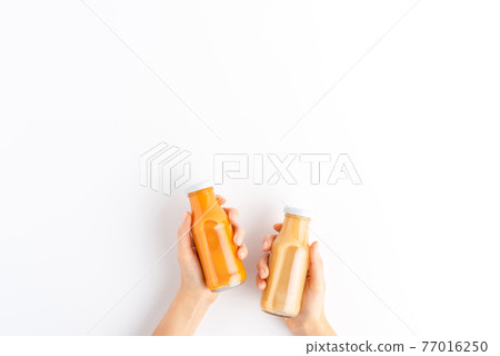 Female hands holding bottles of fruit and vegetable smoothies isolated on white background with copyspace. Top view 77016250