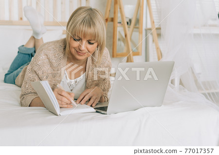 Woman writes in notebook with laptop Woman writes in notebook with laptop 77017357