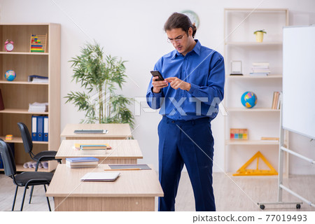 Young male teacher holding smartphone during lesson 77019493