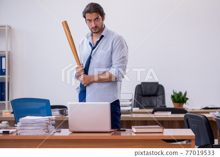 Young male furious employee holding baseball bat in the office Young male furious employee holding baseball bat in the office 77019533