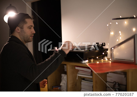 Young unshaven handsome hipster guy puts tonearm on vinyl record on turntable Young unshaven handsome hipster guy puts tonearm on vinyl record on turntable 77020187