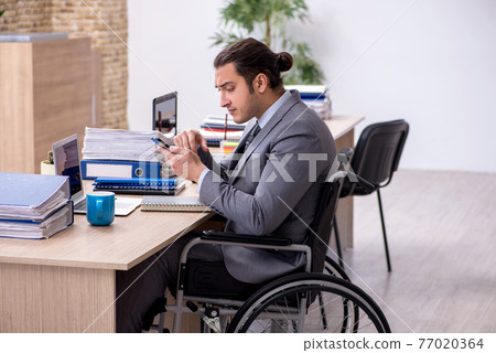 Young male enployee in wheel-chair at workplace Young male enployee in wheel-chair at workplace 77020364