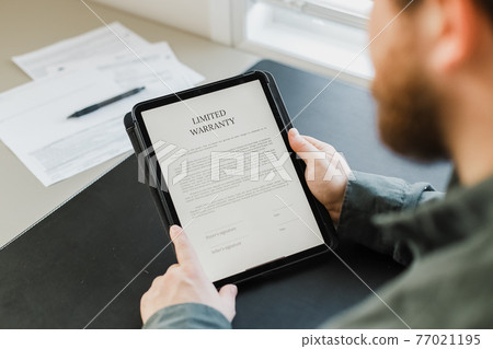 Close up man reading limited warranty tamplate on tablet. 77021195
