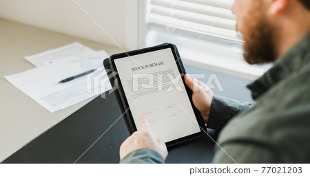 Man reading stock purchase agreement on tablet. 77021203