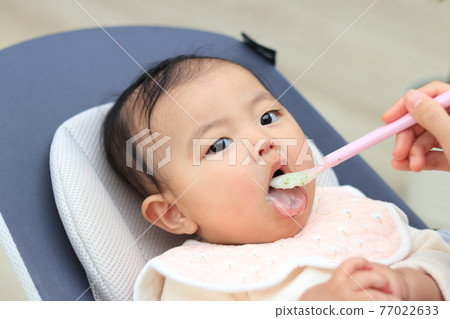 Baby feeding baby food in the living room 77022633