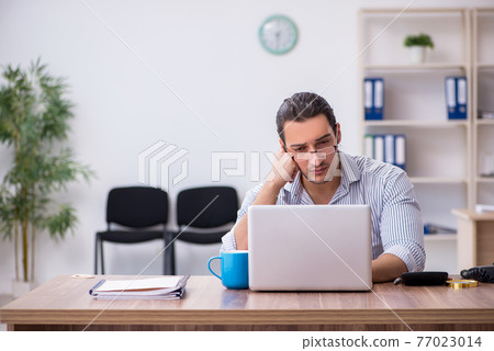Young male bookkeeper working in the office Young male bookkeeper working in the office 77023014