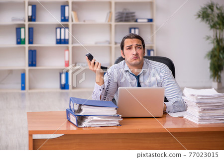 Young male employee unhappy with excessive work in the office Young male employee unhappy with excessive work in the office 77023015