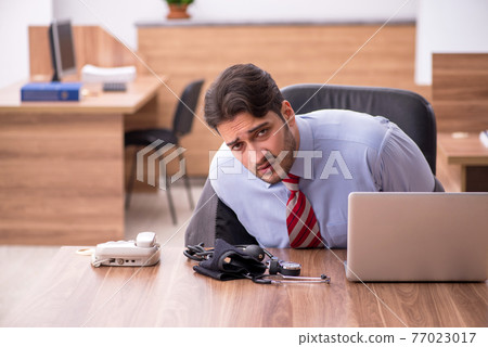 Young male employee suffering from hypertension at workplace 77023017