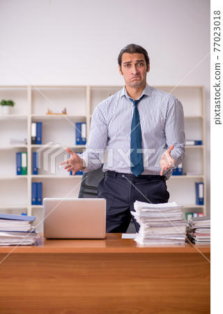 Young male employee unhappy with excessive work in the office Young male employee unhappy with excessive work in the office 77023018