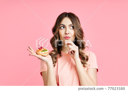 Dieting concept, confused pretty woman looking up holding pastry cake in hand 77023380
