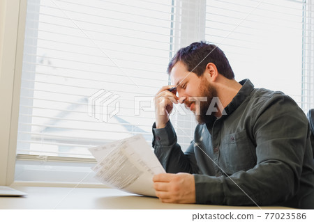 Successful economist reading and filling documents at office near window., 77023586