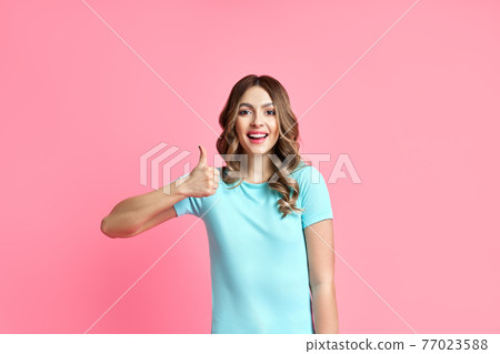 Happy smiling female showing thumbs up on pink background 77023588
