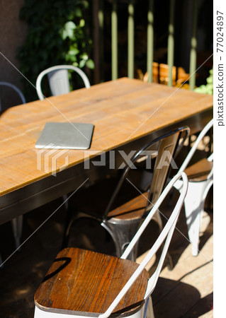 Image of table with closed laptop and chairs near it at cafe. 77024897
