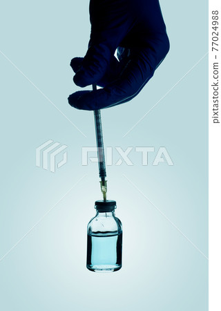 filling a syringe with a blue vaccine 77024988