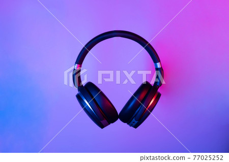 Black wireless bluetooth headphones on neon light background. Music concept. 77025252