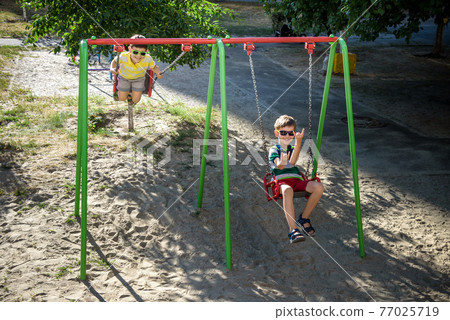 Two little kid boys having fun with swing on outdoor playground. 77025719
