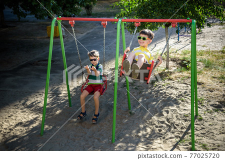 Two little kid boys having fun with swing on outdoor playground. 77025720