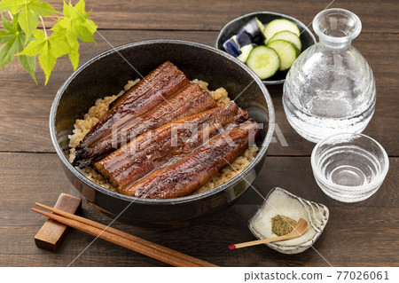 Unadon in a black bowl, sake and green leaves placed on a wooden table Unadon in a black bowl, sake and green leaves placed on a wooden table 77026061