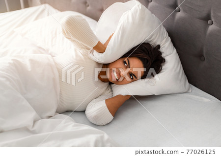 Stressed angry black woman covering ears lying in bed Stressed angry black woman covering ears lying in bed 77026125