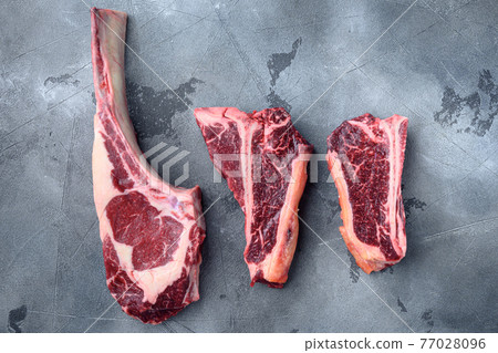 Black Angus Prime raw beef dry aged steak, tomahawk, t bone or porterhouse and club steak, on gray stone background, top view flat lay Black Angus Prime raw beef dry aged steak, tomahawk, t bone or porterhouse and club steak, on gray stone background, top view flat lay 77028096