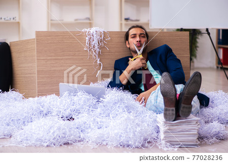 Young male employee and a lot of cut papers in the office Young male employee and a lot of cut papers in the office 77028236