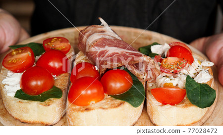 Woman waiter holding a wooden tray with bruschetta in her hand 77028472