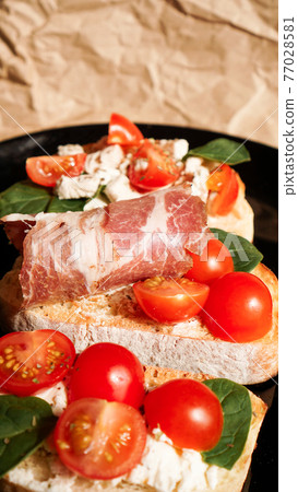 Three bruschetta on a black plate on craft paper. Vertical photo Three bruschetta on a black plate on craft paper. Vertical photo 77028581
