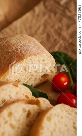Ciabatta slices and cherry tomatoes on craft paper. Ciabatta slices and cherry tomatoes on craft paper. 77028662