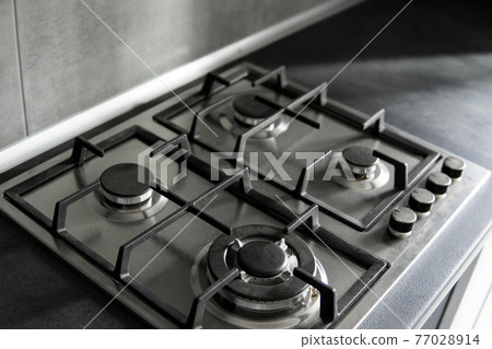 Stainless grey metal kitchen gas stove installed on a the kitchen with a dark grey table top. Stainless grey metal kitchen gas stove installed on a the kitchen with a dark grey table top. 77028914